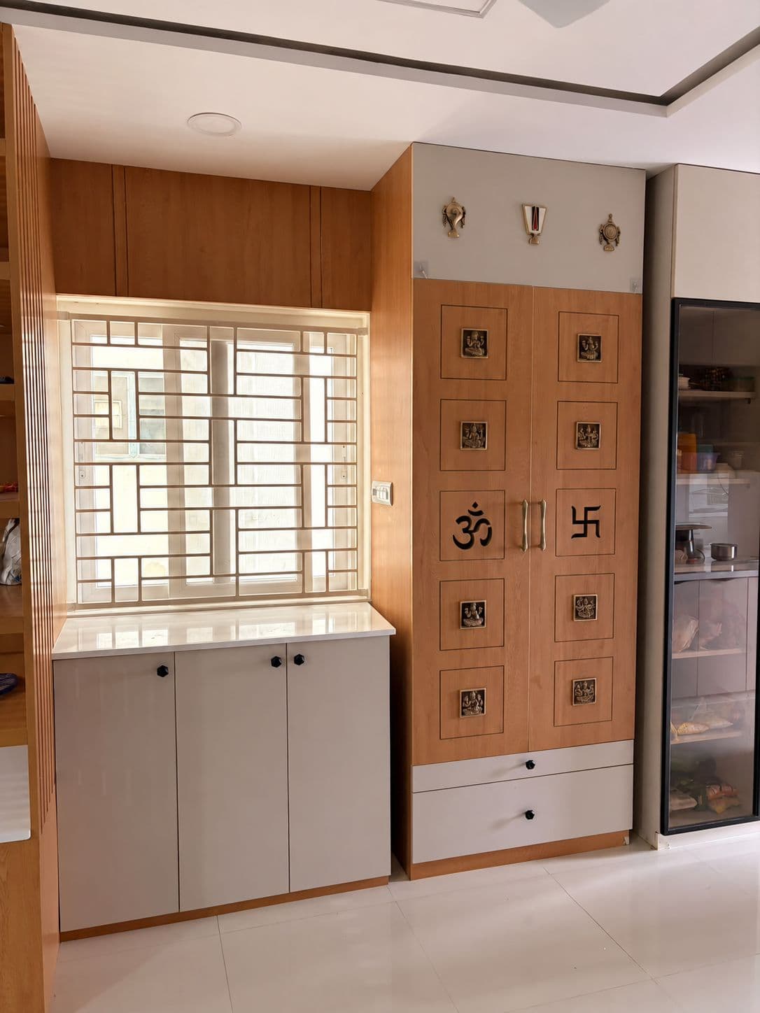 Built-in puja unit with a carved jali window and storage cabinets